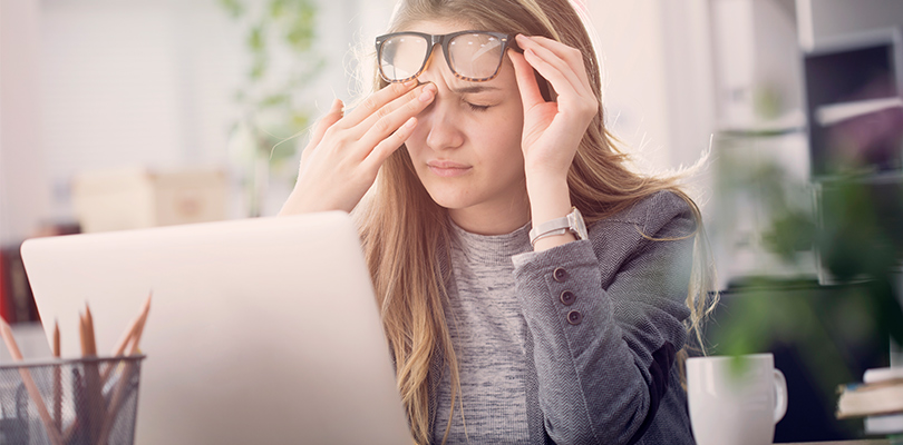 Woman wearing glasses in front of laptop and rubbing forehead